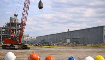 Construction crew observing a fall protection demonstration as a large crane drops a sandbag from height to show impact risk